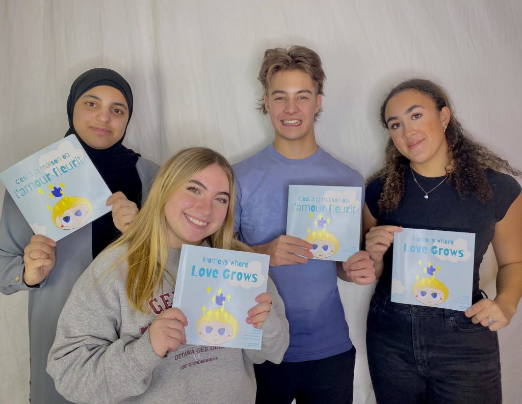 Raya, Federica, Noah, and Ella stand in front of a white background holding their book up to the camera