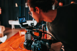 Filmmaker looks through the viewfinder on his camera as he films a scene